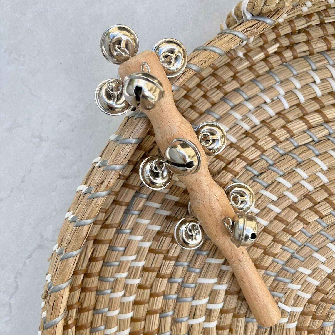 Wooden bell shaker in a woven basket on a light gray background