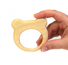 A hand holding a light natural wood bear-shaped teether ring against a plain white background.