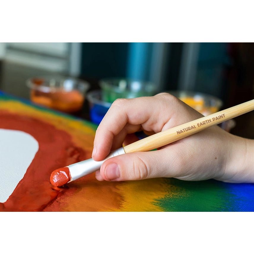 Hand holding a paintbrush with 'Natural Earth Paint' on a colorful painting.