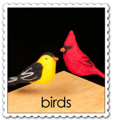 Felted yellow goldfinch and red cardinal hovering over a wooden surface with a black background