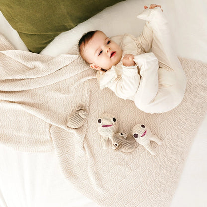 Baby laying on a bed with a green pillow and tan blanket next to two crocheted teeth-shaped and one mouse toy
