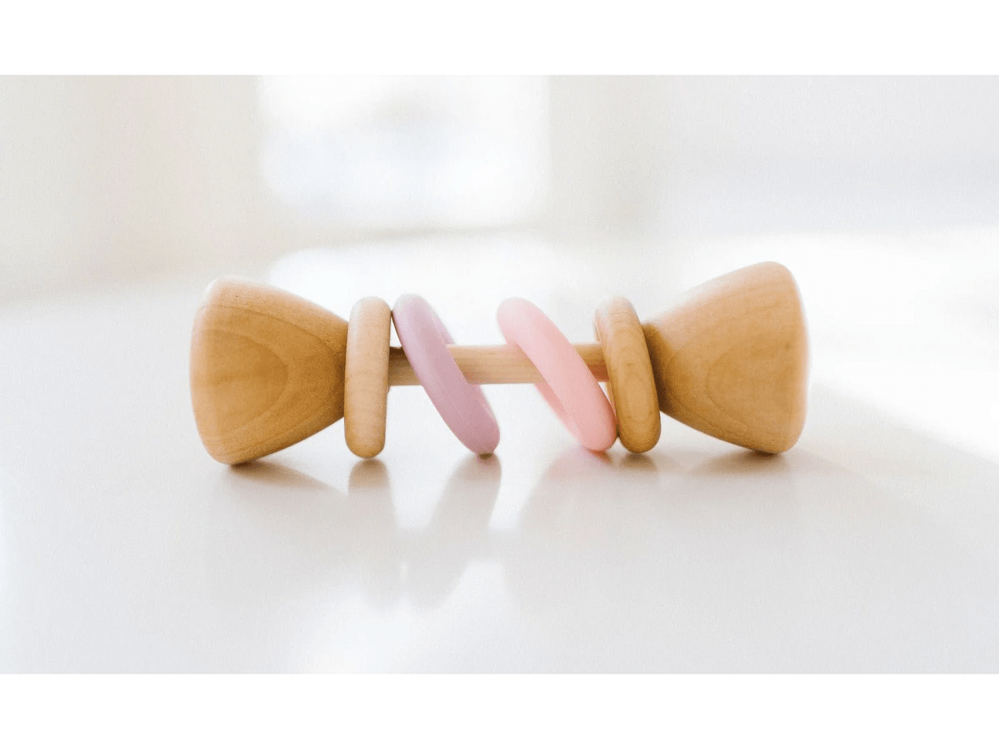 Wooden baby rattle with pink and purple accents on a white background