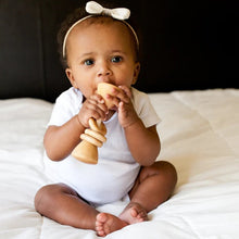 Baby sitting on a bed holding a wooden rattle