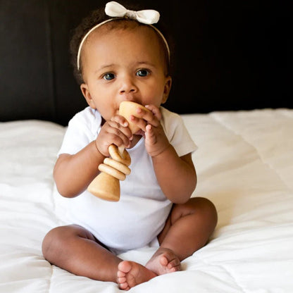 Baby sitting on a bed holding a wooden rattle