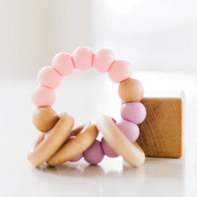 Pink silicone teether with wooden rings on a white background