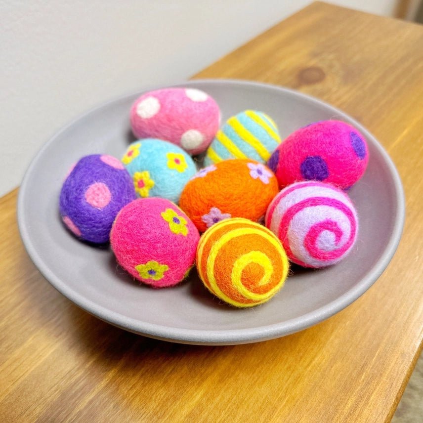 Colorful felted eggs with dots, stripes, and floral patterns on a gray plate on a wooden surface