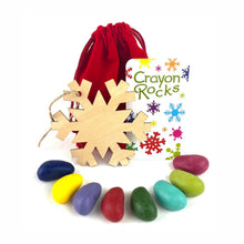 Crayon Rocks branding with 8 rock-shaped crayons, a red velvet bag, and a wooden snowflake ornament on a white background