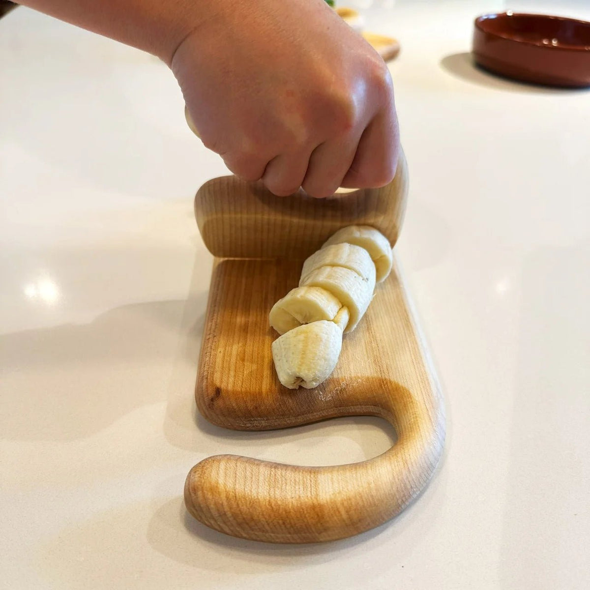 Wooden tool being used to slice bananas on a white surface