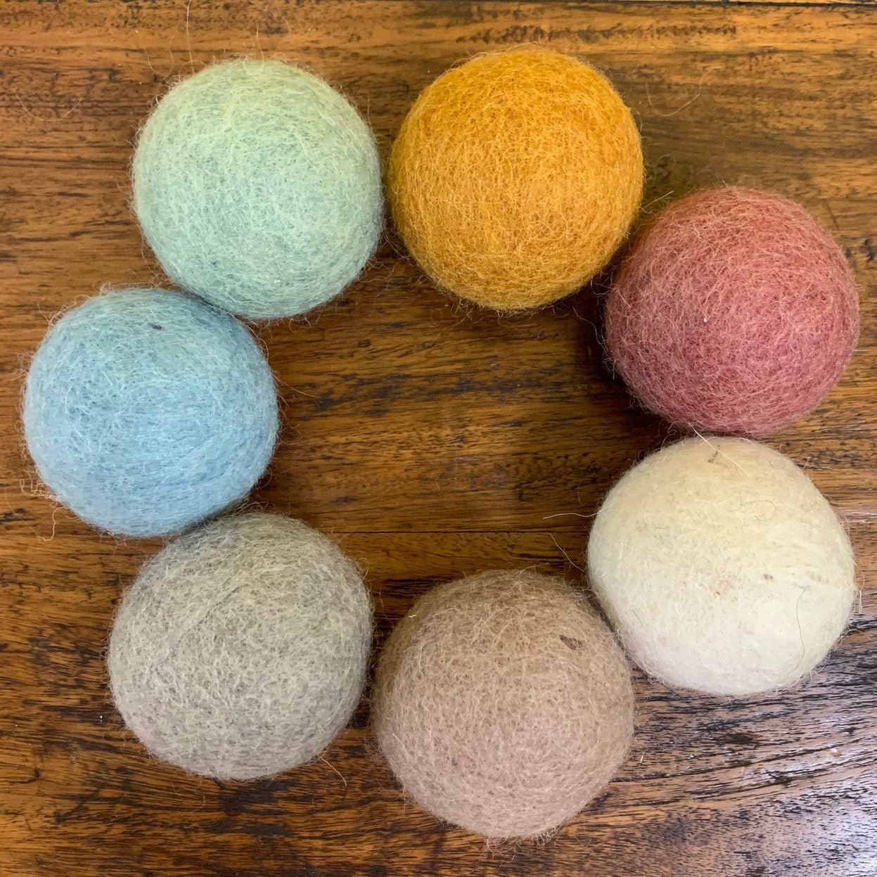 7 felt balls in earth tones arranged in a circle on a wood surface