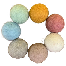 7 felt balls in earth tones arranged in a circle on a wood surface