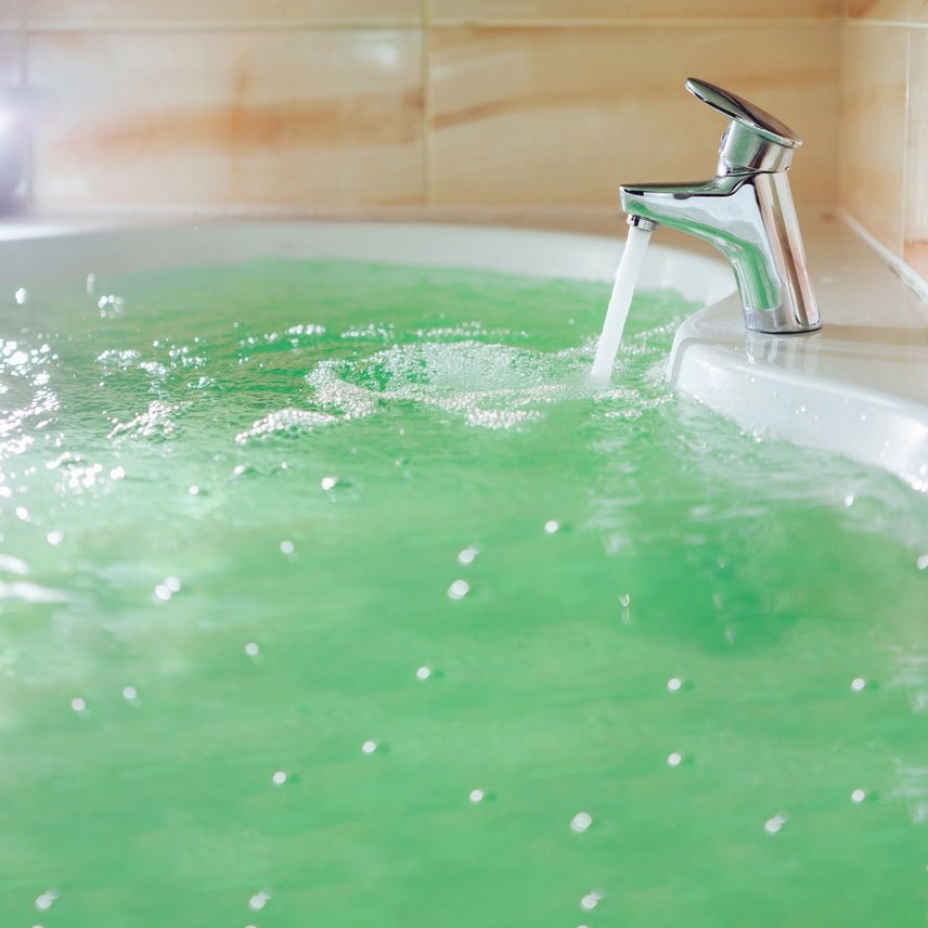 Chrome faucet pouring water into a white bathtub filled with green water