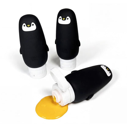 Three penguin-shaped silicone bottles, one is on its side dripping yellow paint on a white background