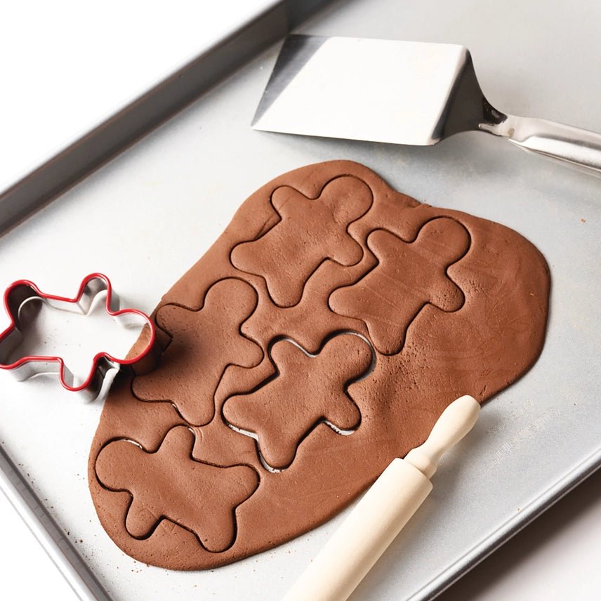 Gingerbread dough with gingerbread man shapes on a baking tray, with a spatula and cookie cutter.