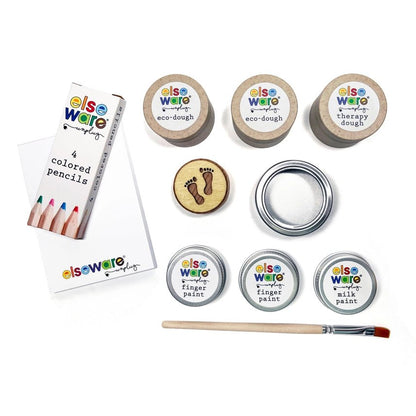 Elseware Unplug colored pencils, paper, eco-dough, therapy dough, finger paint, milk paint, silver tin, wooden stamp, and paintbrush laid out on a white background