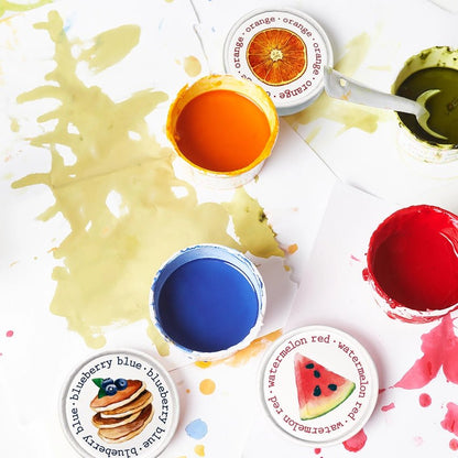 Four colors of finger paint in red, orange, blue, and green in containers, with splattered on paper