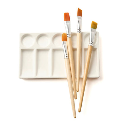White ceramic paint palette with four paintbrushes lying on top on a white background