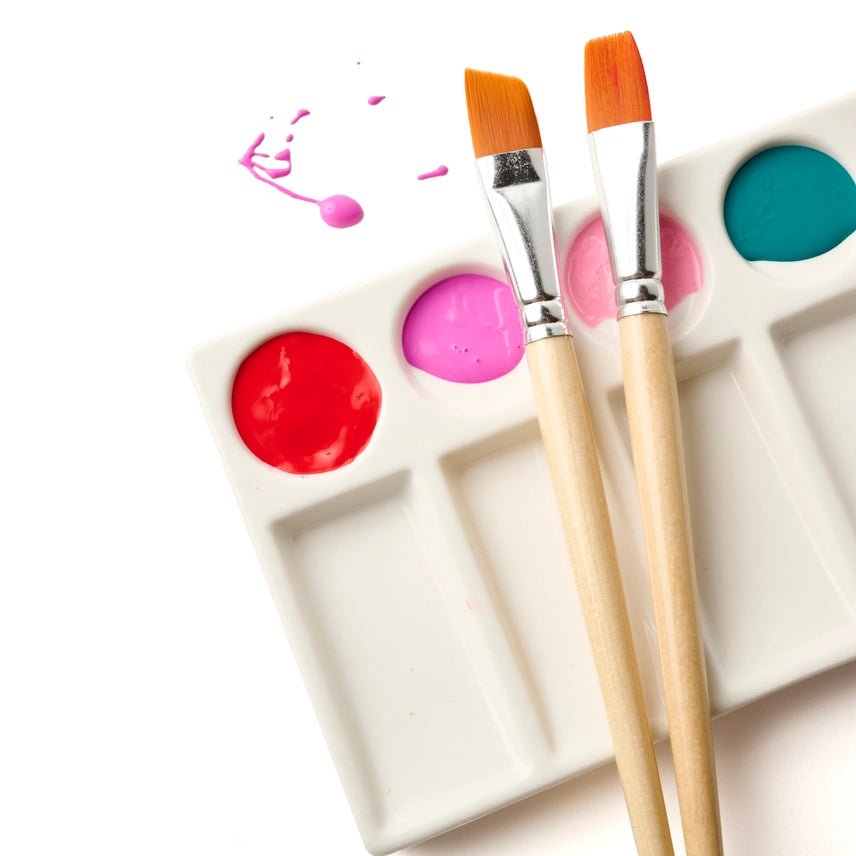 white paint palette with two paint brushes lying on top with paint splatter on a white surface