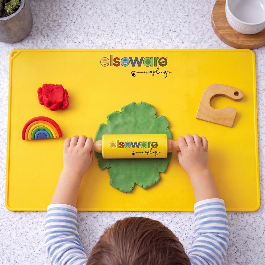 Child rolling out playdough on a yellow silicone