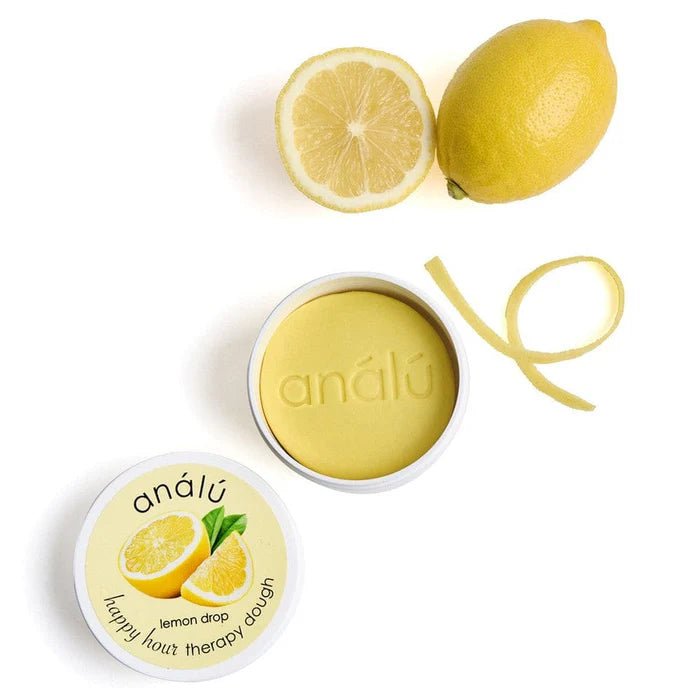 Lemon Drop Therapy dough surrounded by lemon and lemon peel on a white background