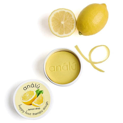 Lemon Drop Therapy dough surrounded by lemon and lemon peel on a white background