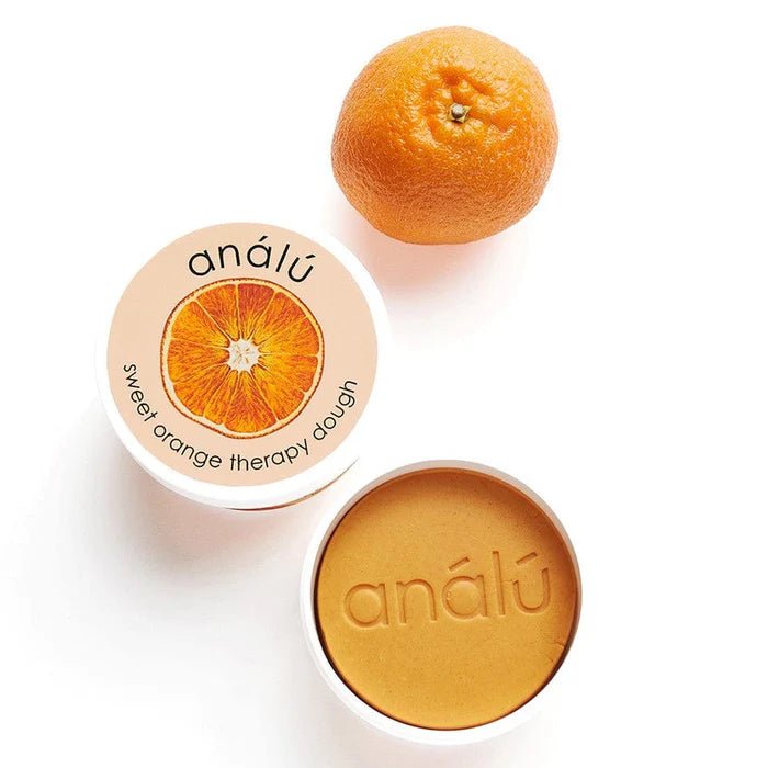 Sweet Orange Therapy dough next to an orange fruit on a white background