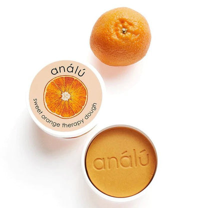 Sweet Orange Therapy dough next to an orange fruit on a white background