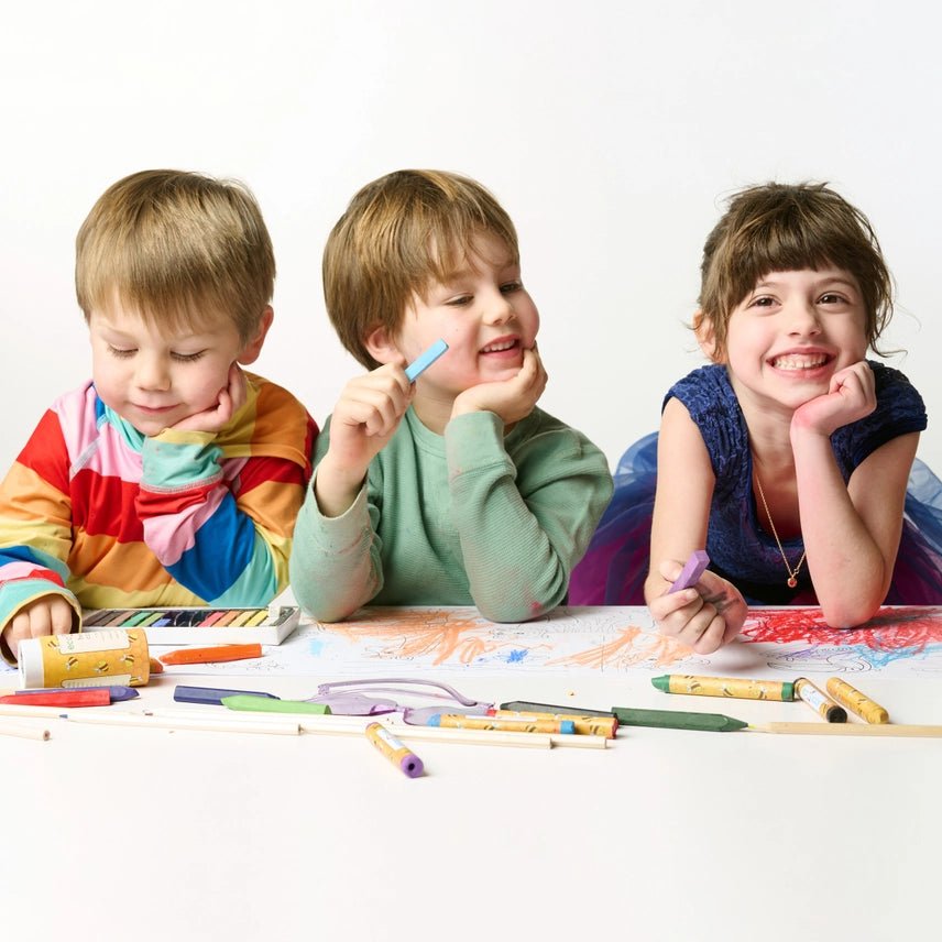 Three children sitting at a table with art supplies, smiling and engaged in an activity.