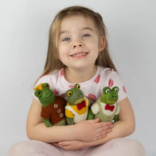 Young girl holding three felted frog dolls against a plain background