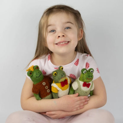 Young girl holding three felted frog dolls against a plain background