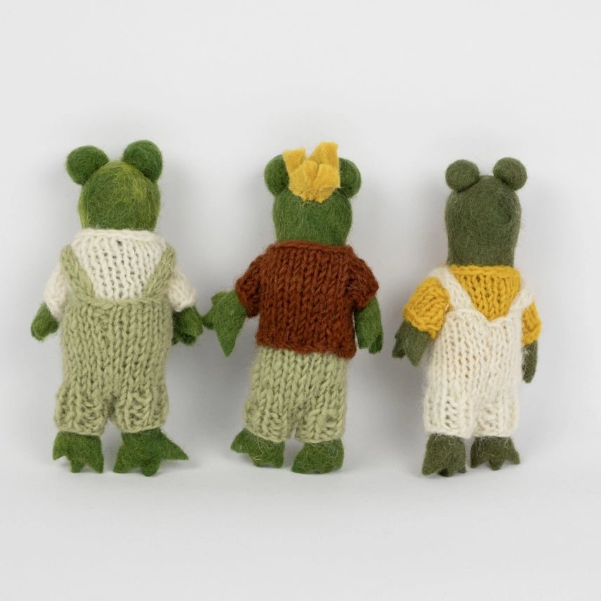 Back view of three felted frog dolls in different outfits on a white background