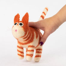A felt needle-art cat toy in orange and cream stripes, held by a human hand against a plain white background.