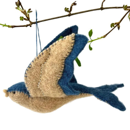 Felted blue bird ornament hanging from a branch on a white background
