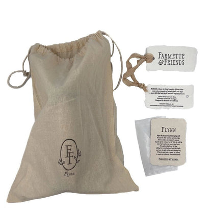 A beige linen drawstring pouch with a custom monogram logo, shown alongside branded paper tags reading 'Farmette & Friends' and 'Flynn'.