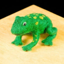 Green needle felted frog with light green spots on a wooden surface against a black background