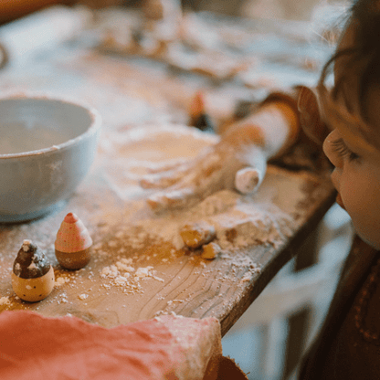 Child playing with flour on a wooden table with a bowl and wooden pastries.