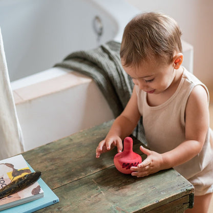 Small child playing with a pink rocking toy on a wooden side table with a bathtub in the background
