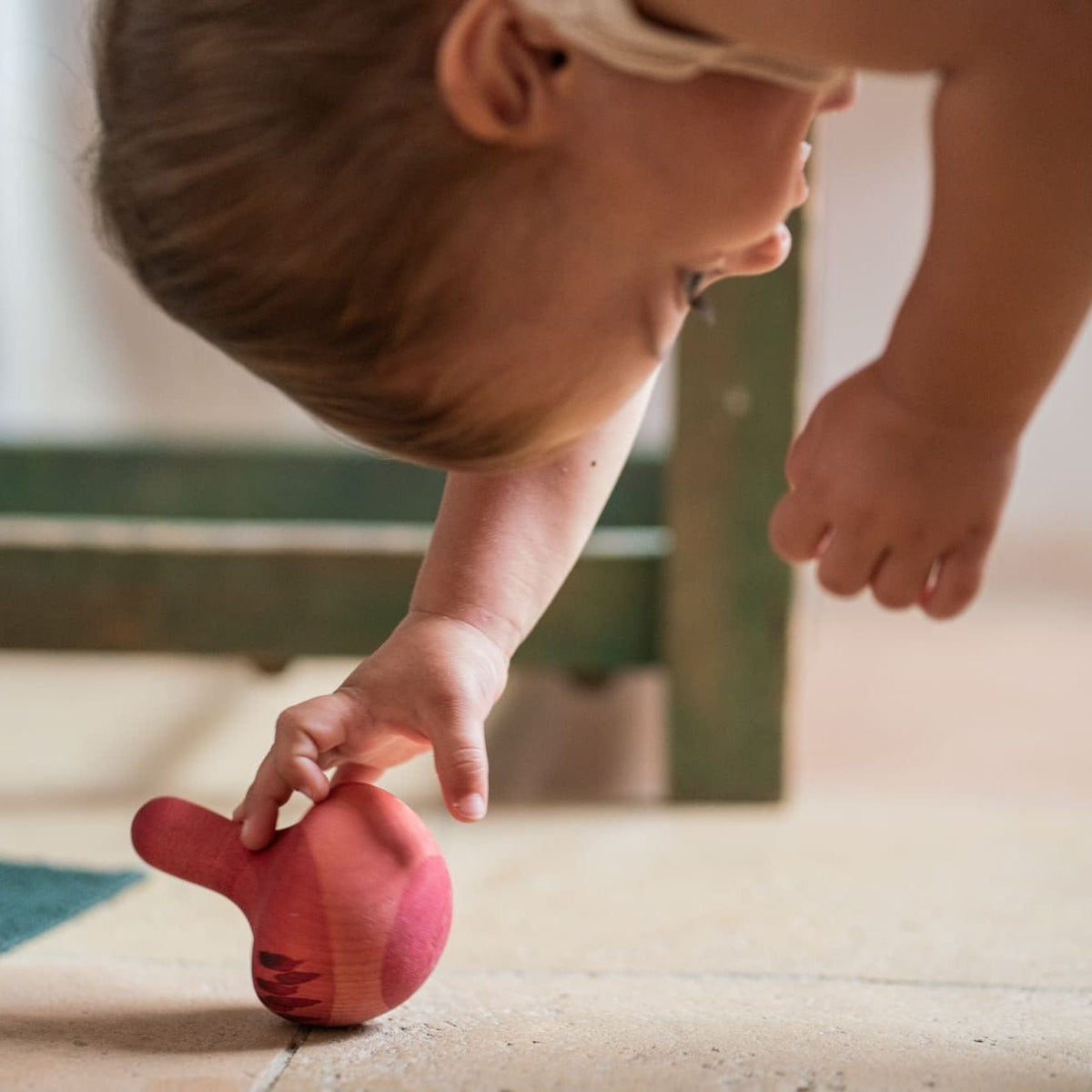 Child playing with a pink rocking toy on a tiled floor