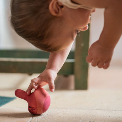 Child playing with a pink rocking toy on a tiled floor
