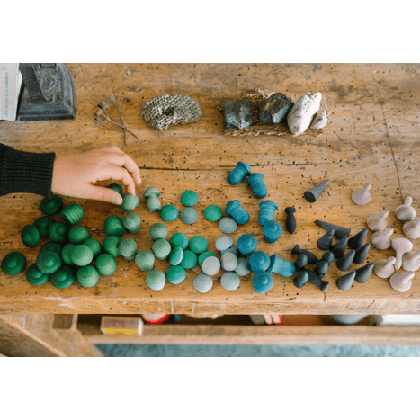 Colorful wooden sculptures on a wooden table with a hand reaching out.