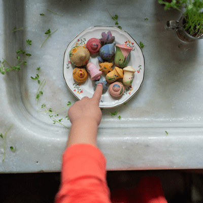 Child's hand pointing to a plate of colorful wooden flowers in a porcelain sink
