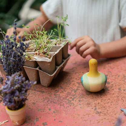 Child's hands interacting with sprouts in cardboard trays with a yellow rocking bird toy sitting on a red metal surface