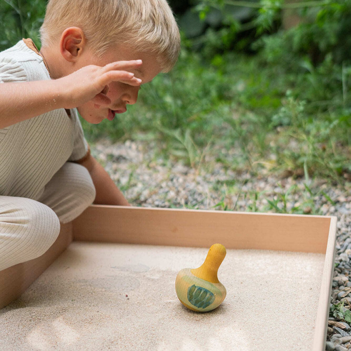 Child playing outside with yellow bird rocking toy in a sand box