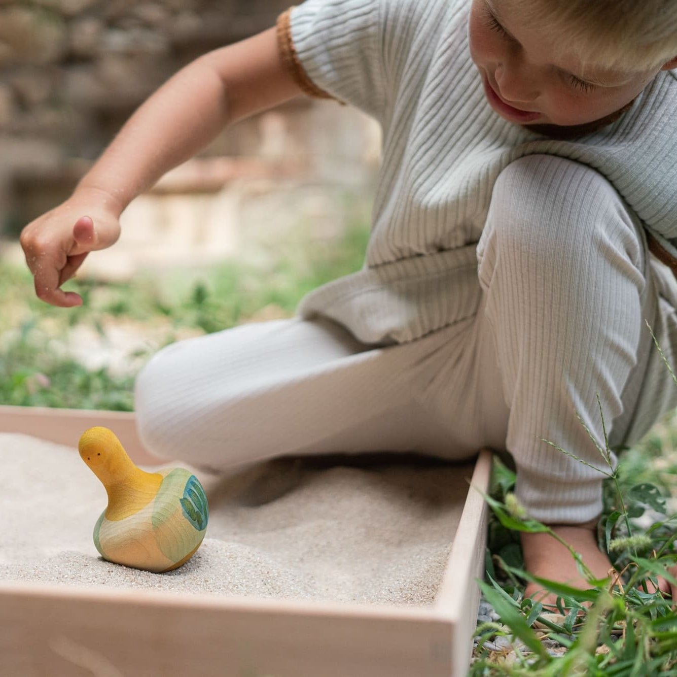 Child playing with yellow bird rocking toy in a sand box outside