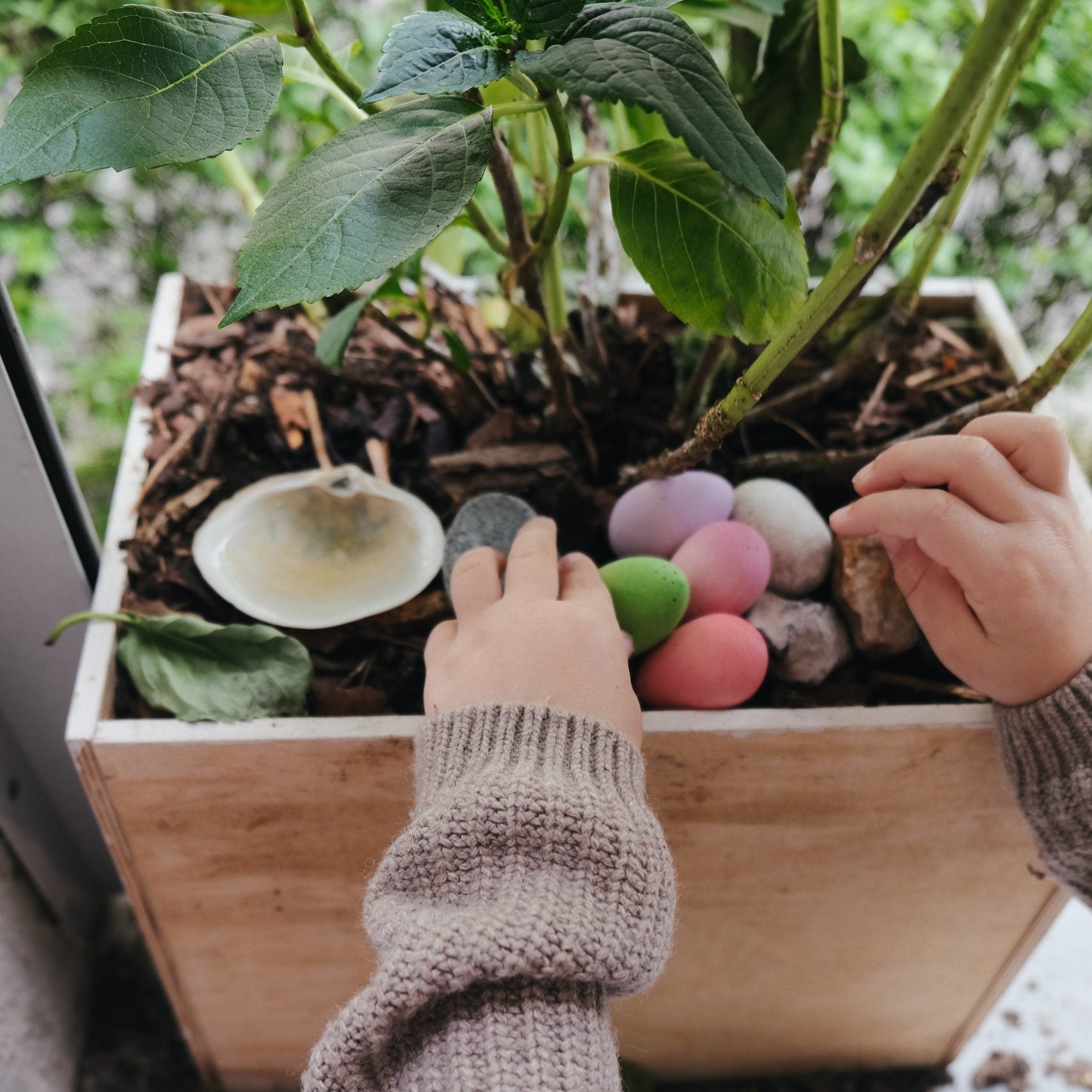 Child interacting with pastel wooden eggs in a planter