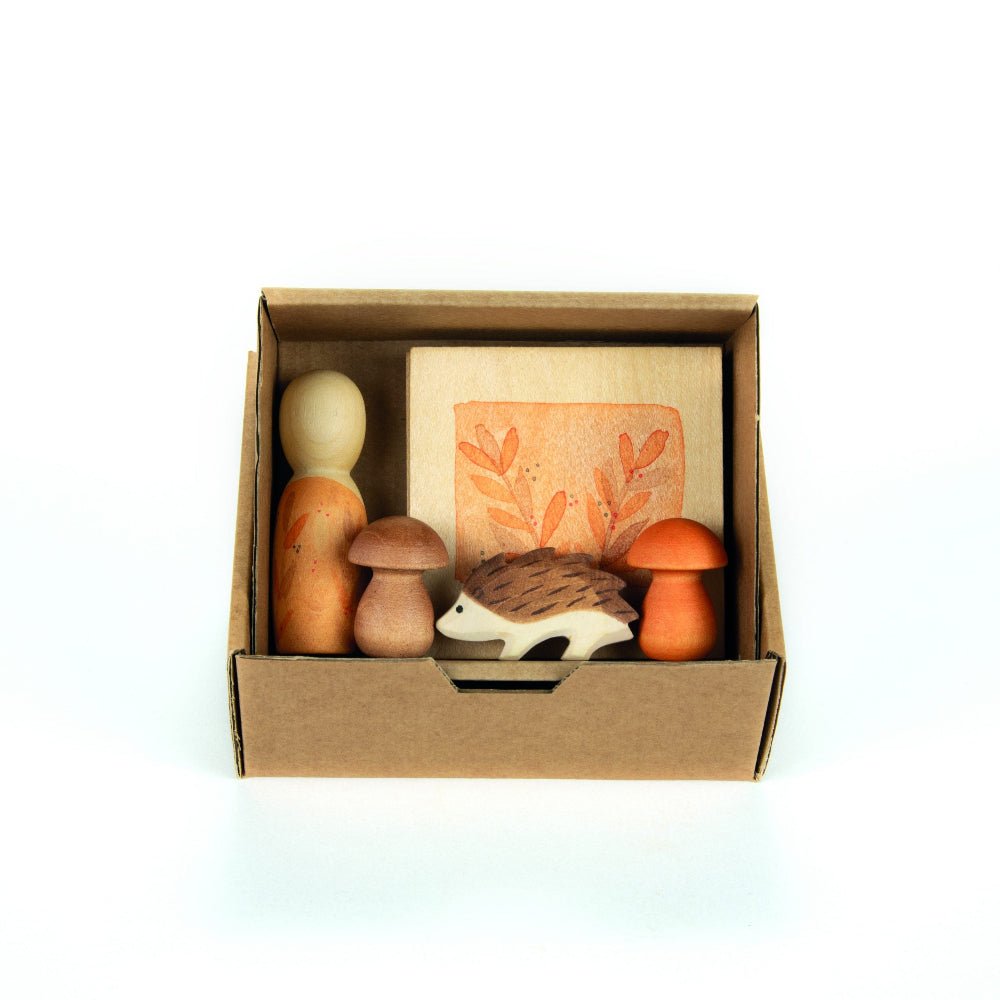 Cardbox containing a wooden nin, mushrooms, and a hedgehog figure on a white background