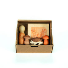 Cardbox containing a wooden nin, mushrooms, and a hedgehog figure on a white background