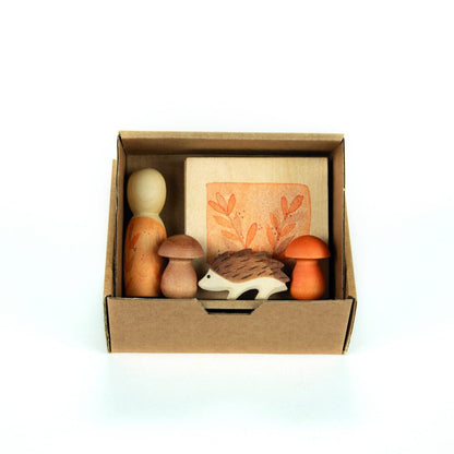 Cardbox containing a wooden nin, mushrooms, and a hedgehog figure on a white background