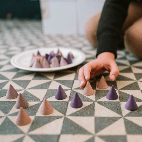 Person playing with pyramid-shaped objects on a geometric-patterned floor.