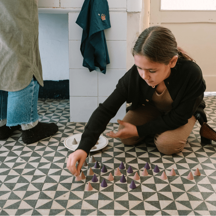 Person playing with pyramid-shaped objects on a tiled floor in a room with a stove and towel.