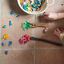 Top down view of child's hands playing with small wooden pieces sorted by color on a tile floor